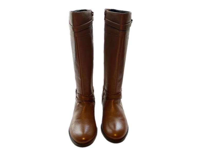 Puede incluir: Un par de botas altas de cuero marr&oacute;n. Cada bota presenta una correa decorativa y detalles de hebilla alrededor del tobillo y la pantorrilla. Las botas tienen una punta redondeada y un tac&oacute;n bajo.