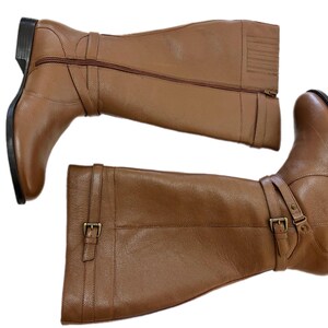Puede incluir: Un par de botas altas de cuero marr&oacute;n. Cada bota tiene una cremallera lateral, una correa con hebilla y un tac&oacute;n bajo. Las botas est&aacute;n dise&ntilde;adas para un look cl&aacute;sico y elegante, adecuado para diversas ocasiones.