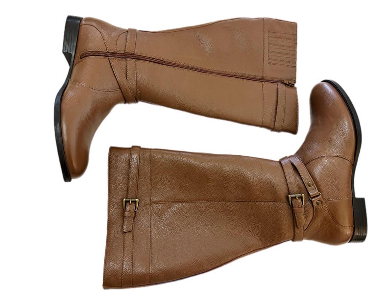 Puede incluir: Un par de botas altas de cuero marr&oacute;n. Cada bota tiene una cremallera lateral, una correa con hebilla y un tac&oacute;n bajo. Las botas est&aacute;n dise&ntilde;adas para un look cl&aacute;sico y elegante, adecuado para diversas ocasiones.