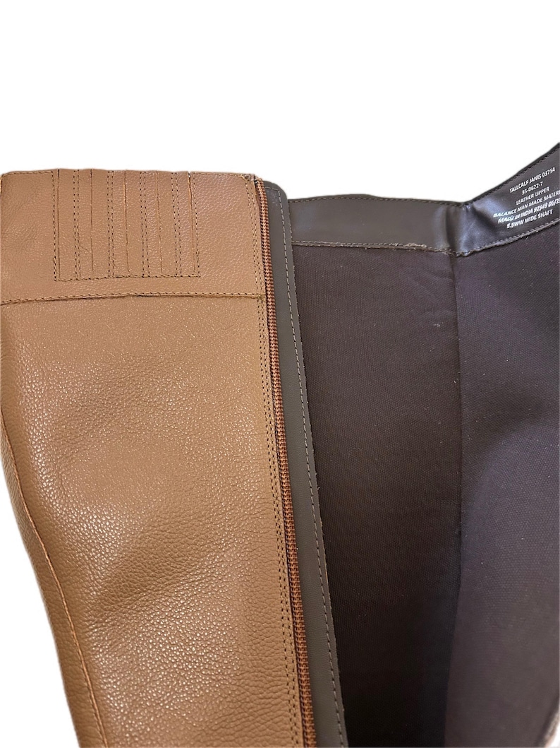 Puede incluir: Primer plano de una bota de cuero marr&oacute;n claro con cremallera. La bota tiene una superficie texturizada y un forro interior marr&oacute;n. La cremallera es de color marr&oacute;n oscuro. La parte superior de la bota tiene costuras decorativas.
