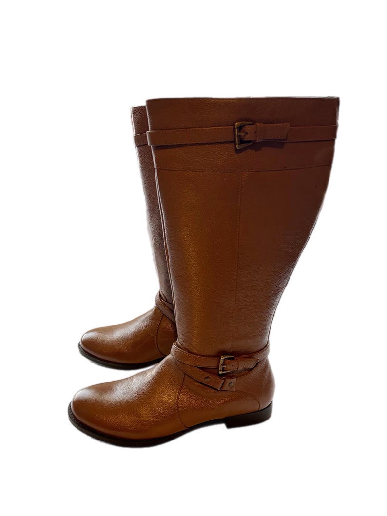 Puede incluir: Un par de botas altas de cuero marr&oacute;n. Cada bota tiene una correa con hebilla alrededor del tobillo y otra en la parte superior. Las botas tienen punta redonda y tac&oacute;n bajo.