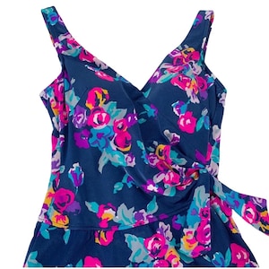 May include: A navy blue swimsuit with a floral print featuring pink, purple, and turquoise flowers. The swimsuit has a V-neckline and a wrap-style bodice with a tie at the side.