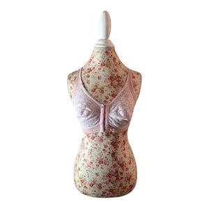 May include: A light pink bra with a front closure, displayed on a floral mannequin. The bra features a delicate lace design and a front closure. The mannequin has a floral pattern.