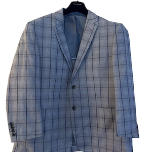 May include: A light blue blazer with a plaid pattern. The jacket has a two-button closure, a notched lapel, and a chest pocket. The sleeves have four buttons at the cuff. The blazer is hanging on a black hanger.