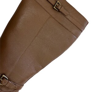 Puede incluir: Primer plano de una bota de montar de cuero marr&oacute;n. La bota presenta una superficie texturizada, una correa con una hebilla dorada en la parte superior y otra hebilla en el tobillo. La bota est&aacute; en &aacute;ngulo, mostrando su dise&ntilde;o.