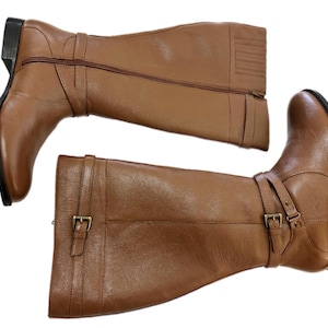 Puede incluir: Un par de botas altas de cuero marr&oacute;n. Las botas tienen una cremallera lateral, una correa con hebilla y un tac&oacute;n peque&ntilde;o. Las botas son de cuero liso.