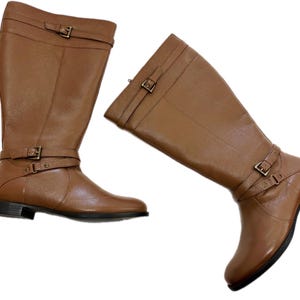 Puede incluir: Dos botas altas de cuero marr&oacute;n. Cada bota tiene detalles de hebilla en el tobillo y otra en la parte superior de la bota. Las botas tienen un tac&oacute;n bajo y una punta redondeada. Las botas son de cuero liso.