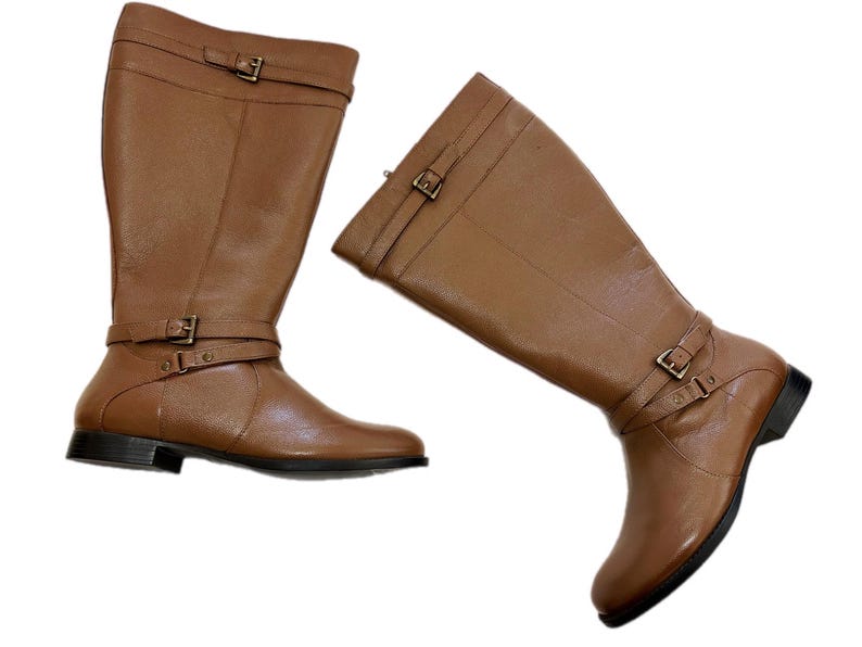 Puede incluir: Dos botas altas de cuero marr&oacute;n. Cada bota tiene detalles de hebilla en el tobillo y otra en la parte superior de la bota. Las botas tienen un tac&oacute;n bajo y una punta redondeada. Las botas son de cuero liso.