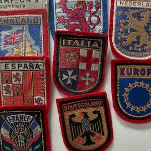 Può includere: Una collezione di toppe ricamate con bandiere ed emblemi di vari paesi. Le toppe hanno bordi rossi e includono le bandiere di Inghilterra, Spagna e Francia, oltre agli emblemi di Italia, Germania e Lussemburgo. Le toppe sono di varie forme.