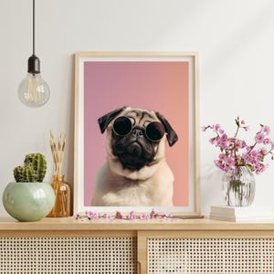 Puede incluir: Una impresión enmarcada que presenta un pug con gafas de sol redondas sobre un fondo degradado rosa y naranja. El pug tiene un pelaje marrón claro con la cara y las orejas negras. La impresión se muestra en un mueble de madera.