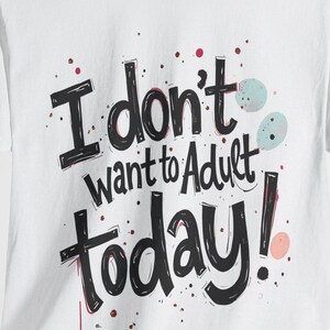 May include: White t-shirt with a black graphic print that says "I don't want to adult today!" with colorful splatters.