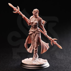 May include: A detailed, light brown figurine of a female elf warrior, holding a spear with a three-pronged head. The figure is clad in armor and a flowing gown, standing on a circular base. The background is dark.