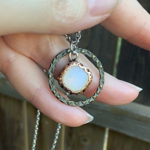 May include: A silver chain necklace with a white opal stone pendant set in a bronze circle with a smaller bronze circle around it.