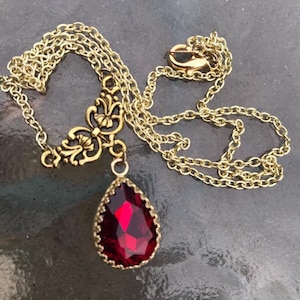 May include: A gold chain necklace with a red teardrop-shaped pendant. The pendant has a gold filigree design around the red stone.