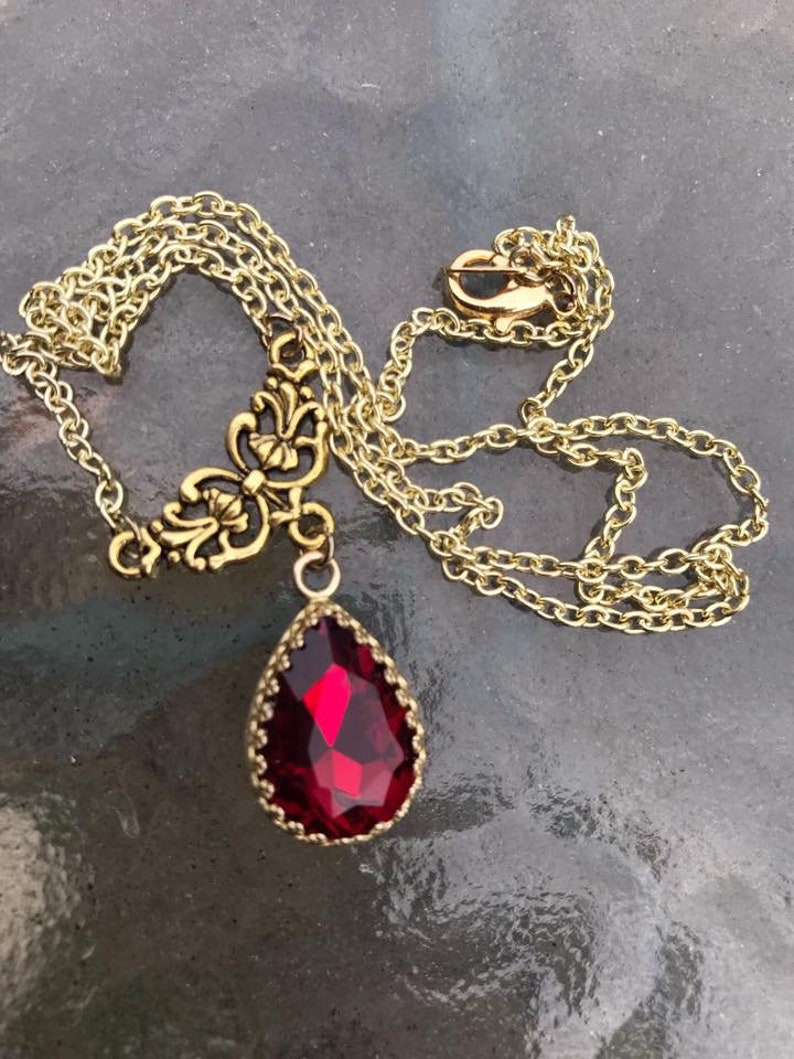 May include: A gold chain necklace with a red teardrop-shaped pendant. The pendant has a gold filigree design around the red stone.