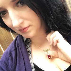 May include: A gold necklace with a teardrop-shaped red gemstone pendant. The pendant has a gold filigree design around the gemstone.
