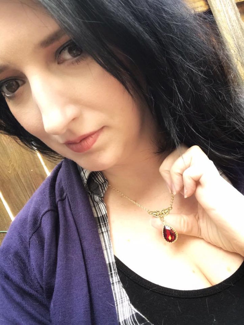 May include: A gold necklace with a teardrop-shaped red gemstone pendant. The pendant has a gold filigree design around the gemstone.