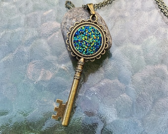 May include: A bronze key pendant necklace with a round, blue, green, and gold glitter charm. The charm is set in a decorative, ornate frame.
