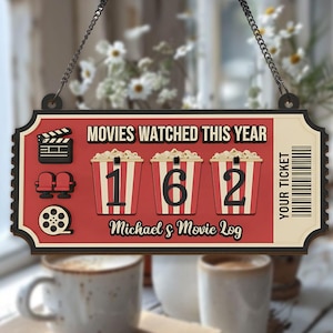 May include: A red and cream-colored movie log sign with the text "MOVIES WATCHED THIS YEAR" and "162" in popcorn buckets. Includes a film reel, clapperboard, and theater seats. The sign reads "Michael's Movie Log" and "YOUR TICKET".