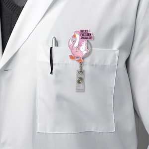 May include: A pink and white badge reel featuring a cartoon goose in a nurse's uniform, complete with a stethoscope and cap. The badge reel has the text "RELAX I'VE SEEN SMALLER!" and is attached to a clear plastic holder.