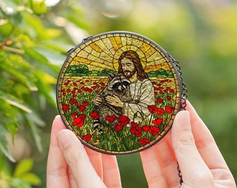 May include: Round stained glass art piece featuring a religious figure embracing a raccoon in a field of red poppies. The artwork has a yellow and gold background with a black metal frame and chain.