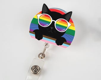 May include: A retractable badge reel featuring a black cat wearing white-framed sunglasses with rainbow lenses. The cat is set against a rainbow background, with a pink and brown stripe at the bottom. The reel has a clear plastic strap and a metal clip.