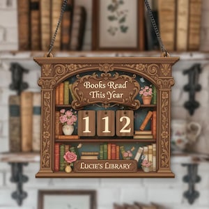 May include: A decorative wooden sign in the shape of a bookshelf, featuring the text "Books Read This Year" and "Lucie's Library." The sign shows the number 112. It is brown with floral and bookshelf details, and has a hanging chain.