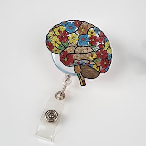 May include: A badge reel with a brain design filled with red, yellow, blue, and brown flowers. The badge reel has a clear plastic strap and a metal clip for attaching to clothing.