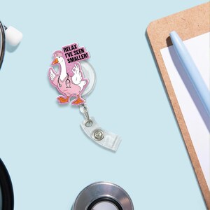May include: A pink and white badge reel featuring a cartoon goose in a nurse's uniform. The goose is giving an 'okay' hand gesture. The badge reel has the text "Relax I've seen smaller!" in pink letters.