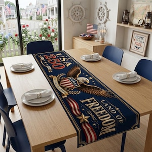 May include: A navy blue table runner with the text "USA 250" and "Land of Freedom" featuring an eagle, stars, and stripes design. The runner is placed on a wooden table set for a meal.