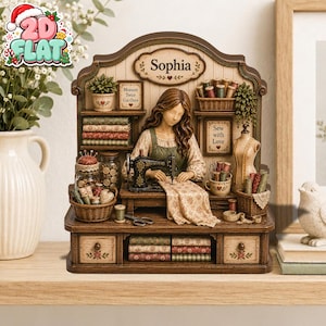 Könnte beinhalten: Ein dekoratives Nähzimmer-Diorama aus Holz mit einer Figur namens Sophia an einer Nähmaschine. Das Stück enthält Regale mit Stoffrollen, eine Schneiderpuppe, Garnkörbe sowie Schilder mit der Aufschrift Measure Twice Cut Once und Sew with Love.