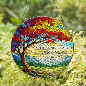 May include: A round stained glass window with a colorful tree design. The tree has red, orange, yellow, and purple leaves. The text reads "50th Anniversary" with names and a date. The background shows a landscape.