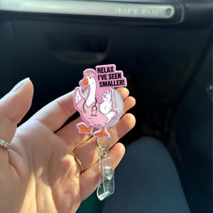 May include: A pink and white badge reel featuring a cartoon goose in a nurse's uniform, with the text "Relax I've seen smaller!". The reel has a clear plastic clip and a retractable cord.