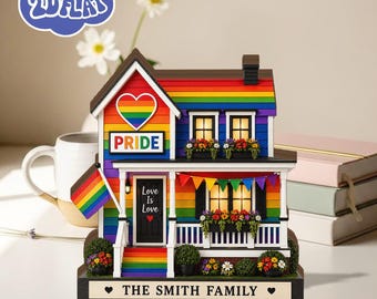 May include: A colorful Pride house figurine with a rainbow roof, heart-shaped logo, and the word "PRIDE". The house has a porch with a banner that says "Love Is Love". The base reads "THE SMITH FAMILY".