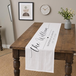 May include: A white table runner with black script that reads "The William" and the names "Sophia & David" with a heart symbol and the date "07.14.2026". The runner is displayed on a wooden table.