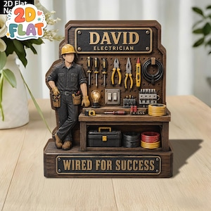 Puede incluir: Un adorno de escritorio decorativo con la figura de un electricista con casco amarillo y ropa de trabajo oscura junto a un panel perforado con herramientas, una bombilla y componentes eléctricos. El texto dice DAVID ELECTRICIAN y WIRED FOR SUCCESS.
