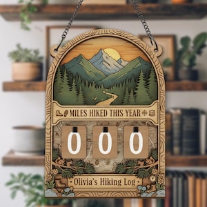 May include: Wooden hiking log with a mountain scene, the text "MILES HIKED THIS YEAR", and the name "Olivia's Hiking Log". The log has three number dials showing "000". The sign is hanging from a chain.