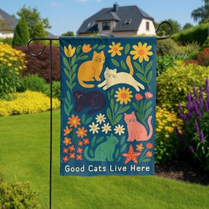 Puede incluir: Una bandera de jardín azul marino con ilustraciones coloridas de gatos y flores. La bandera tiene el texto "Good Cats Live Here" en la parte inferior. Los gatos son de varios colores, incluyendo naranja, blanco, negro, verde y rosa. Las flores son amarillas, naranjas y blancas.