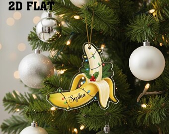 May include: A novelty Christmas tree decoration in the shape of a peeled banana, adorned with fairy lights and the name "Sophia". The ornament is yellow and white, with a gold hanging string. The text "2D FLAT" is in the upper left corner.