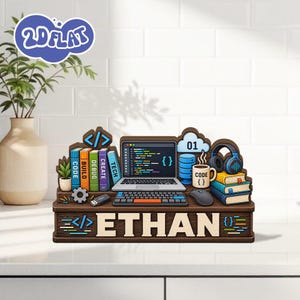 May include: A wooden desk organizer featuring a laptop, keyboard, mouse, headphones, and books labeled CODE, BUILD, DEBUG, CREATE, and TECH. The base displays the name ETHAN in large letters, flanked by blue coding symbols and a cloud icon with 01.