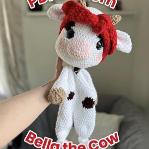 May include: A white crochet cow plush toy with brown spots, a pink snout, and blue eyes, wearing a red headband. The text PDF Pattern and Bella the Cow are visible in red letters against the white background of the plush toy image.