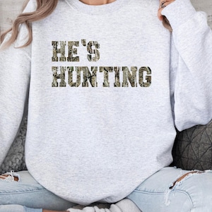 May include: A gray sweatshirt with the text "HE'S HUNTING" in camouflage print.