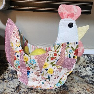 May include: A handmade fabric chicken-shaped basket with a patchwork design. The basket features pink, white, and floral patterned fabrics, a black button eye, and a yellow beak. It is filled with yellow pears.