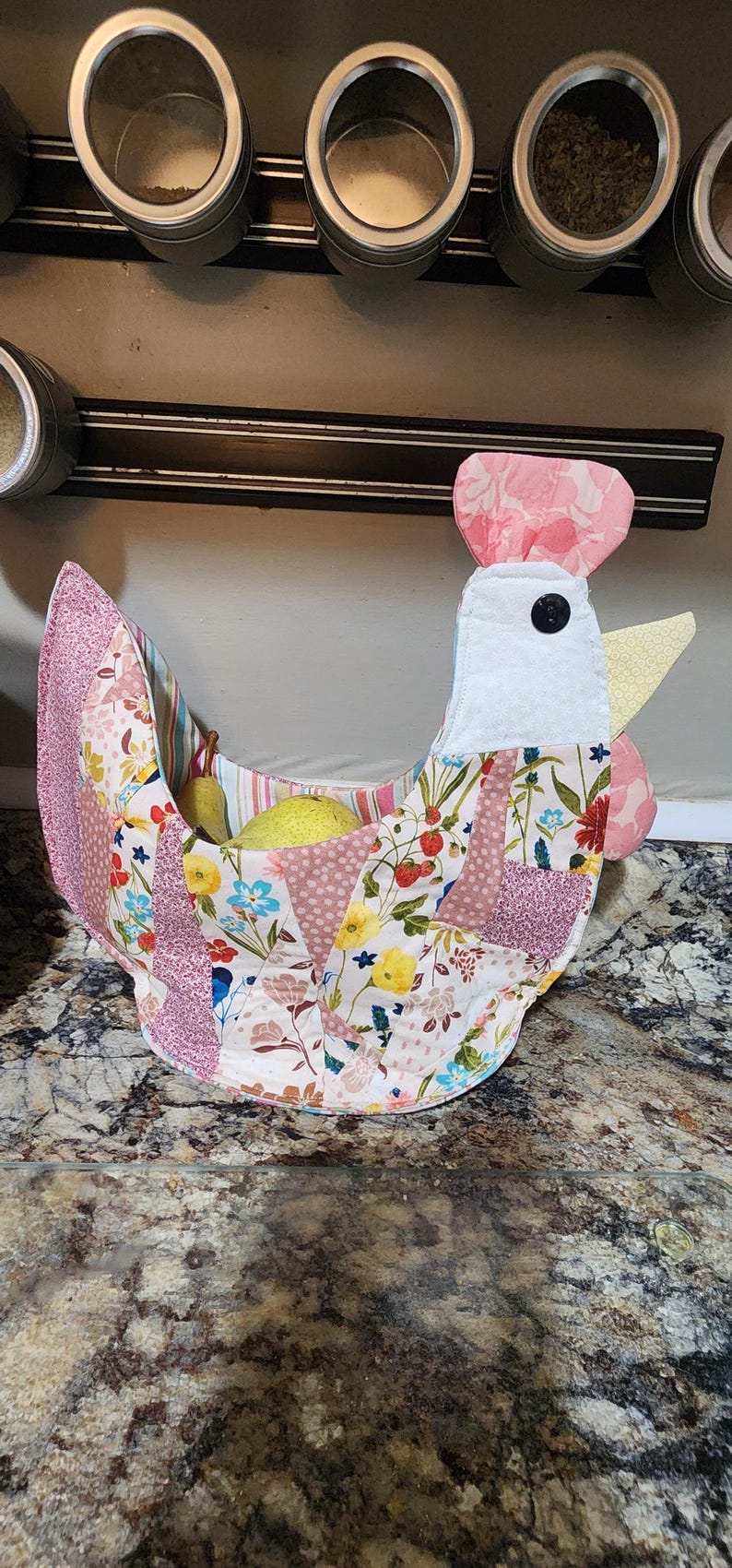 May include: A handmade fabric chicken-shaped basket with a patchwork design. The basket features pink, white, and floral patterned fabrics, a black button eye, and a yellow beak. It is filled with yellow pears.