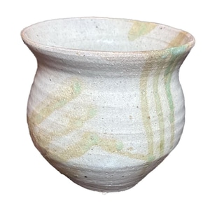 May include: A handmade, off-white ceramic bowl with a rounded body and flared rim. The bowl features subtle, textured horizontal lines and is adorned with streaks of pale yellow and green glaze, creating a rustic aesthetic.