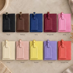 May include: Ten rectangular passport holders with matching luggage tags, each featuring a gold-tone buckle. The colors include black, brown, navy, burgundy, pink, ivory, blush, lemon, purple, and sunset rose, arranged in two rows of five.