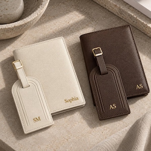 May include: A cream passport holder with the name Sophia and a matching luggage tag with the initials SM, alongside a dark brown passport holder with the initials AS and a matching luggage tag with the initials AS, all featuring gold text.