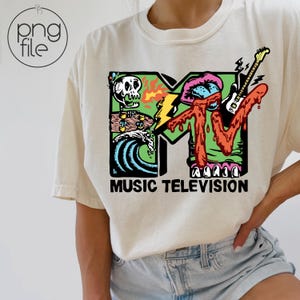 May include: Cream-colored t-shirt featuring a colorful graphic of the MTV logo with a skull, waves, lightning bolt, and guitar. The words "MUSIC TELEVISION" are printed below the logo in black.