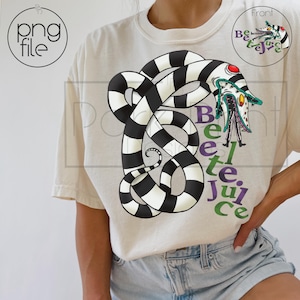 Pode incluir: Camiseta creme com um desenho de cobra listrada em preto e branco e as palavras "Beetle Juice" em verde e roxo. O desenho inclui um rosto de desenho animado. Uma versão menor do desenho está no canto superior direito.