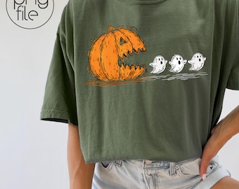 May include: Olive green t-shirt featuring a Halloween-themed graphic. The design includes an orange pumpkin with a jagged mouth, appearing to eat three small white ghosts. The graphic is a playful and spooky illustration.